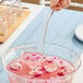 A clear plastic disposable ladle being used to serve pink punch from a decorative bowl.