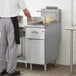 A man in a white shirt and black apron using a stainless steel gas fryer to cook food.