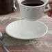 A person holding a Tuxton eggshell swirl rim saucer with a cup of coffee on it.