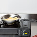 A Vollrath stainless steel fry pan with a black silicone handle on a stove.