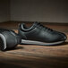 A pair of black Shoes For Crews Avery non-slip athletic shoes on a wood floor.