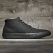 A black Shoes For Crews Cabbie II men's shoe with a black rubber sole on a wood surface.