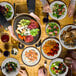 A table with a group of people eating salad from cream melamine bowls with brown trim.