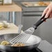 A Victorinox slotted turner with a black handle flipping food in a pan.