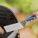 A hand using a Dexter-Russell high heat blue steak turner over a grill.