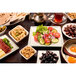 A white glazed deep square melamine bowl filled with food on a table with plates of food.