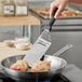 A hand using a Victorinox square edge turner to cook food in a pan.