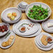 A stack of GET Pottery Market melamine bowls with white trim on a table with plates and bowls of food.