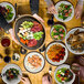 A table with a bowl of salad with shrimp and tomatoes, a plate of pasta with chicken and vegetables, and a bowl of sauce.
