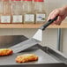 A person using a Victorinox round edge turner with a black handle to cut food on a griddle.