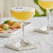 An Acopa Empire coupe glass filled with yellow liquid on a table.