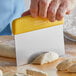 A person using a Dexter-Russell bench scraper with a yellow handle to cut dough.