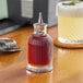 A Barfly ribbed glass bitters bottle on a table with liquid inside.