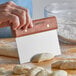 A person using a Dexter-Russell bench scraper to cut dough.