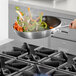 A person cooking vegetables on a Cooking Performance Group liquid propane range.