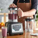 A person in an apron using an AvaMix commercial blender to make a smoothie.