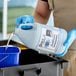 A person in blue gloves pouring Noble Chemical Actifoam concentrated restroom cleaner into a white container.