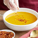 A person pouring Regal Mild Crushed Red Pepper into a bowl of soup.