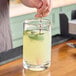 A person pouring a drink into a Barfly heavy-duty mixing glass on a counter in a cocktail bar.