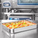 A Vollrath stainless steel roasting pan filled with food on a counter.