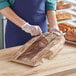 A person wearing gloves putting a loaf of bread in a Choice kraft paper bag with a wheat design window.