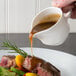 A person pouring LeGout beef gravy on a plate of meat with broccoli and carrots.