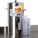 A stainless steel Bunn 3 gallon iced tea dispenser with clear plastic cups and lids.