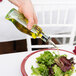 A hand pouring Tablecraft olive oil into a salad on a table.