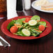 A cranberry melamine bowl filled with salad and a sandwich on a table.