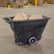 A black Rubbermaid tilt truck with a hinged dome lid full of cardboard boxes.