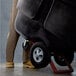 A person pushing a black Rubbermaid tilt truck with a hinged dome lid.