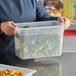 A person holding a Cambro translucent polypropylene food pan filled with broccoli.