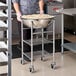 A man in a chef's uniform using a Choice stainless steel mixing bowl stand with a large metal bowl.