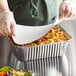 A person in gloves holding a Choice oblong foil container with a paper lid over food.