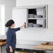 A woman wearing a chef hat opening a Regency stainless steel wall cabinet with plates in it.