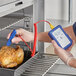 A person holding a Comark PK19M thermometer to measure the temperature of a chicken over a grill.