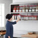 A woman in a chef's hat reaching for spices on a Regency stainless steel wall shelf.