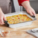 A hand using a Choice Heavy-Duty Foil Steam Pan to serve food.