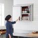 A woman opening a Regency stainless steel wall cabinet filled with jars of spices.