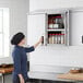 A woman opening a Regency stainless steel wall cabinet filled with jars of spices.