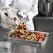 A person in a white coat preparing food in a Choice shallow foil steam table pan on a counter.