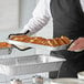 A person holding a Choice shallow foil steam table pan of food on a table at a catering event.