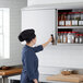 A woman in a chef's hat opening a Regency stainless steel wall cabinet with spices.