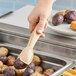 A person using Cambro beige plastic tongs to scoop potatoes into a pan.