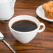 An Arcoroc white oversized cup of coffee next to a muffin on a table.