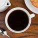 An Arcoroc oversized cup of coffee and a cookie on a table.