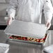 A chef holding a full size metal tray with food inside.