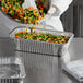 A person pouring mixed vegetables from a bowl into a Choice foil steam pan.