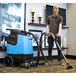 A man in a brown shirt using a Mytee Speedster heated carpet extractor to vacuum a carpet.