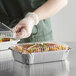 A person in gloves holding a tray of food in a Choice foil container.